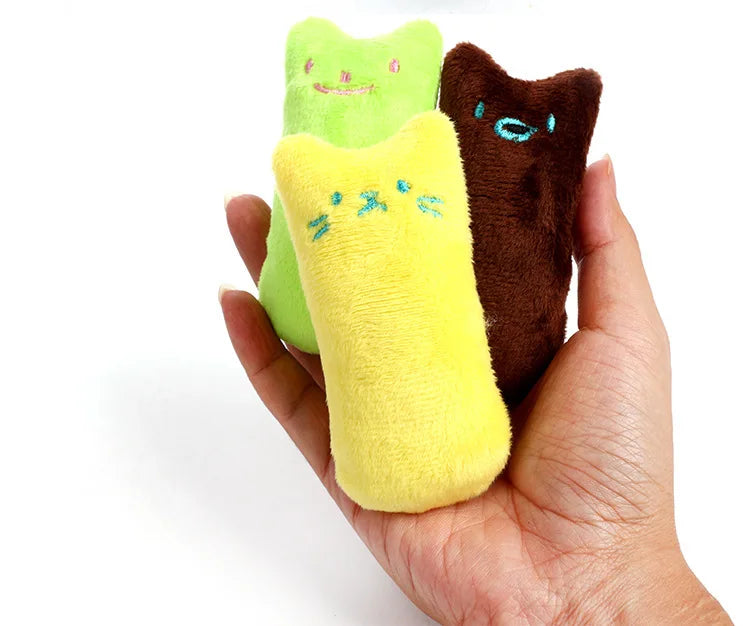 Trois jouets en peluche pour chat, jaune, vert et marron, tenus dans le creux d'une main pour montrer leur petite taille