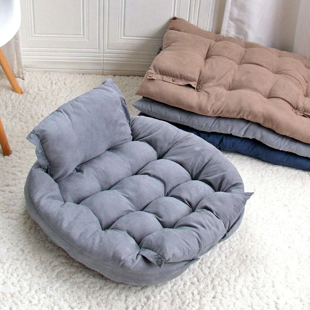 Coussin couchage gris replié en corbeille avec dossier, posé sur un tapis blanc à côté de matelas empilés
