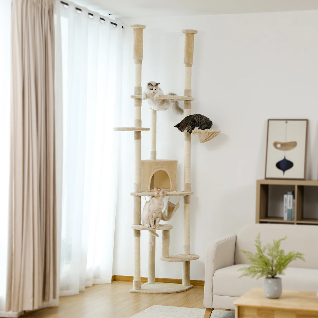 Grand arbre à chat beige dans un salon lumineux, avec trois chats installés sur les plateformes et dans le hamac