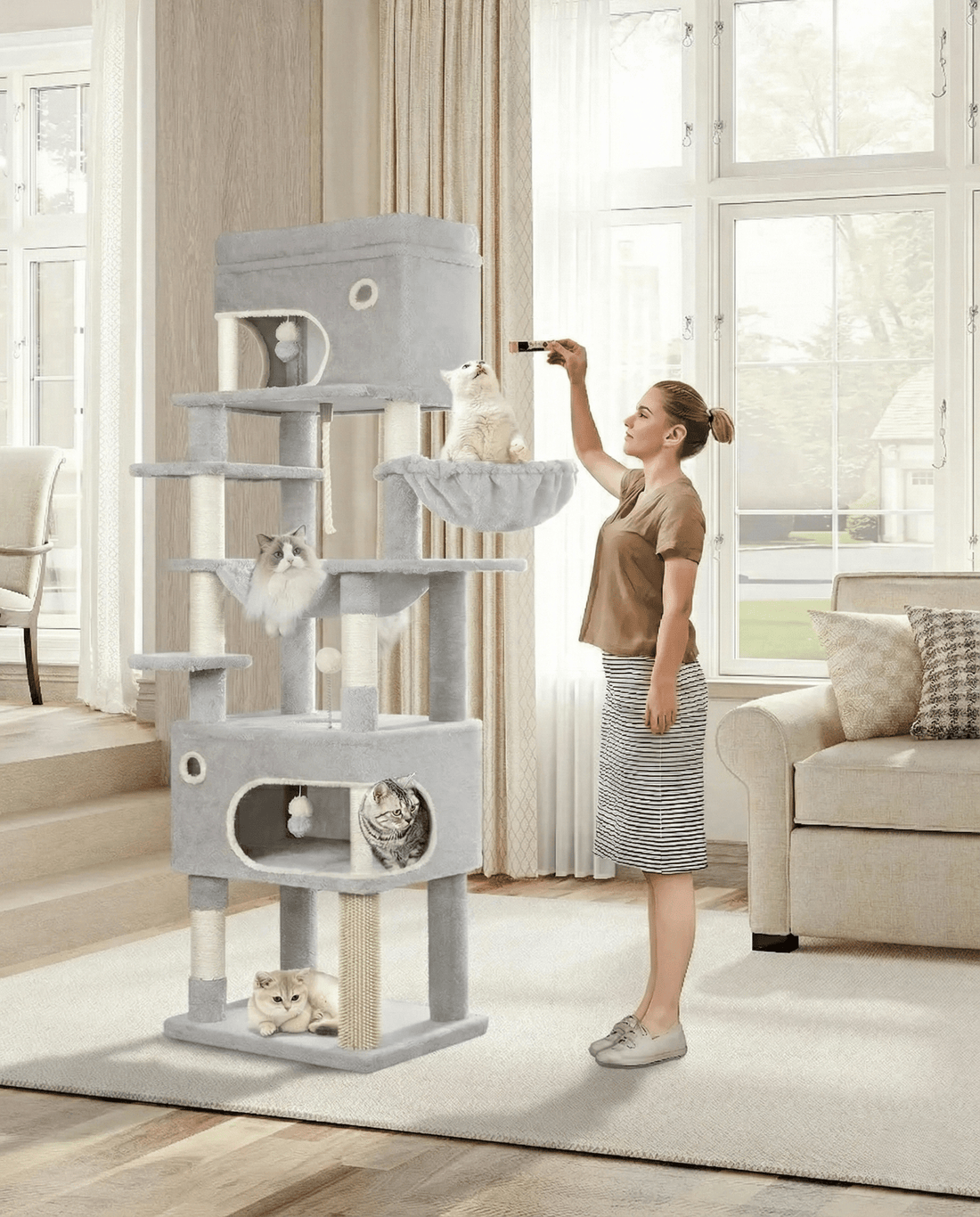 Femme jouant avec un chat sur le grand arbre à chat gris, où trois autres chats se reposent dans le salon