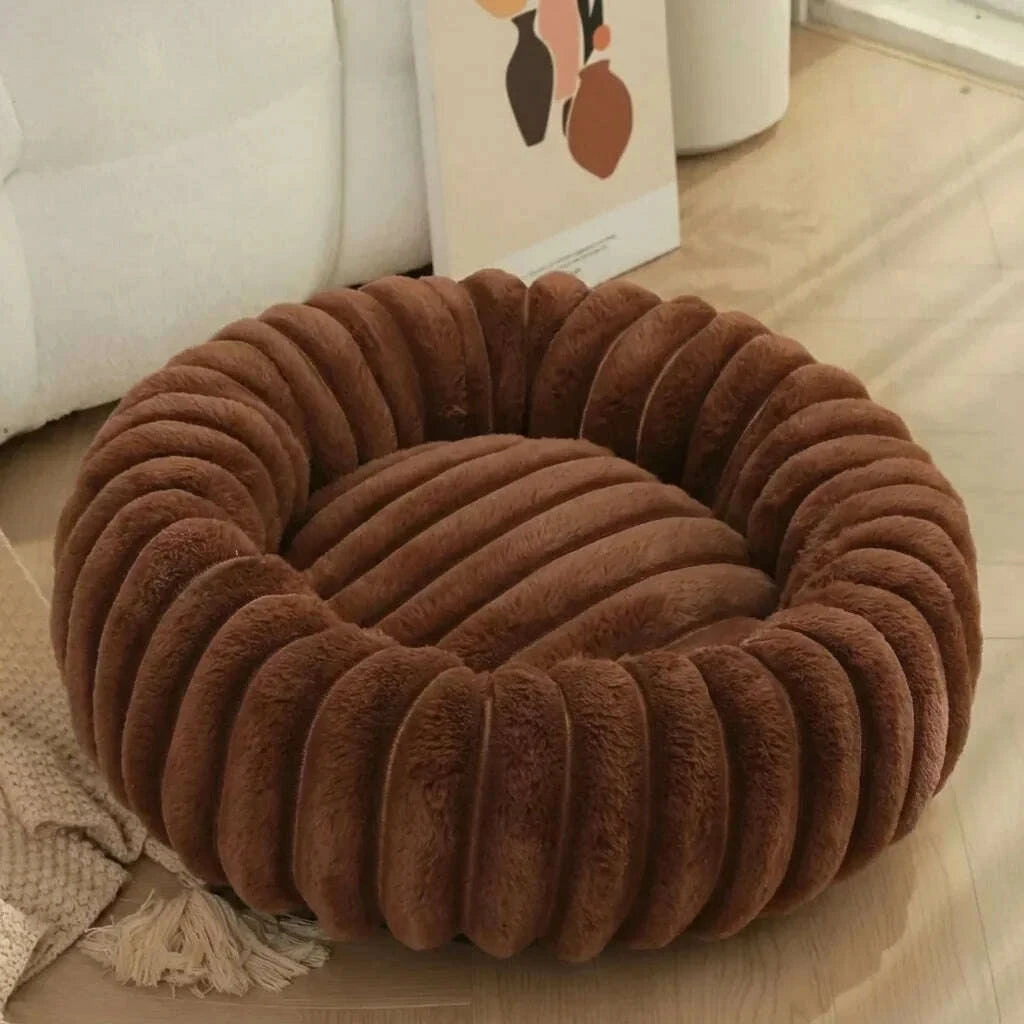 Corbeille marron en peluche côtelée au centre plat, posée sur un parquet clair près d'un canapé blanc