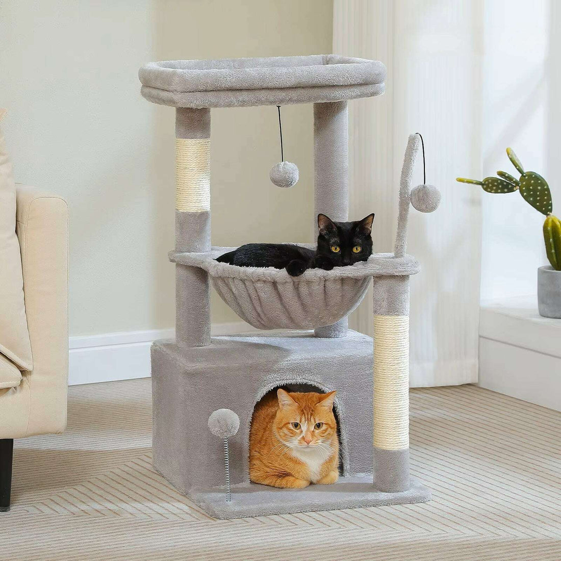 Meuble à chat gris clair dans un salon lumineux, chat noir dans le hamac et chat roux dans la niche