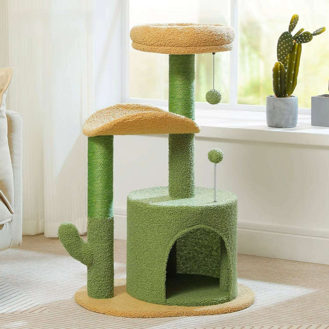Arbre à chat vert et beige à niche, poteaux en sisal et pompons suspendus, près d'une fenêtre