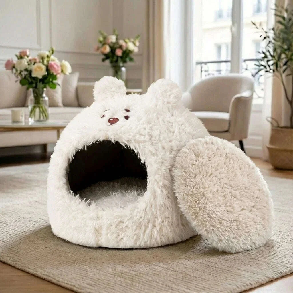 Niche ourson blanche pour chat, coussin rond retiré à côté, dans un salon avec fauteuil et fleurs