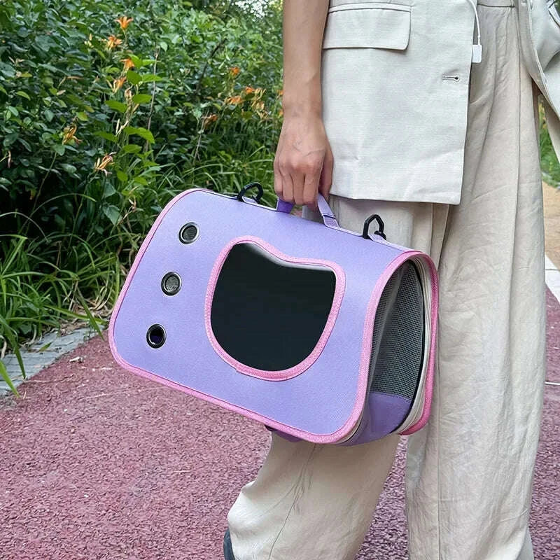 Main tenant un sac de transport violet clair pour chat, bordure rose, aération en filet et hublot, sur allée rouge