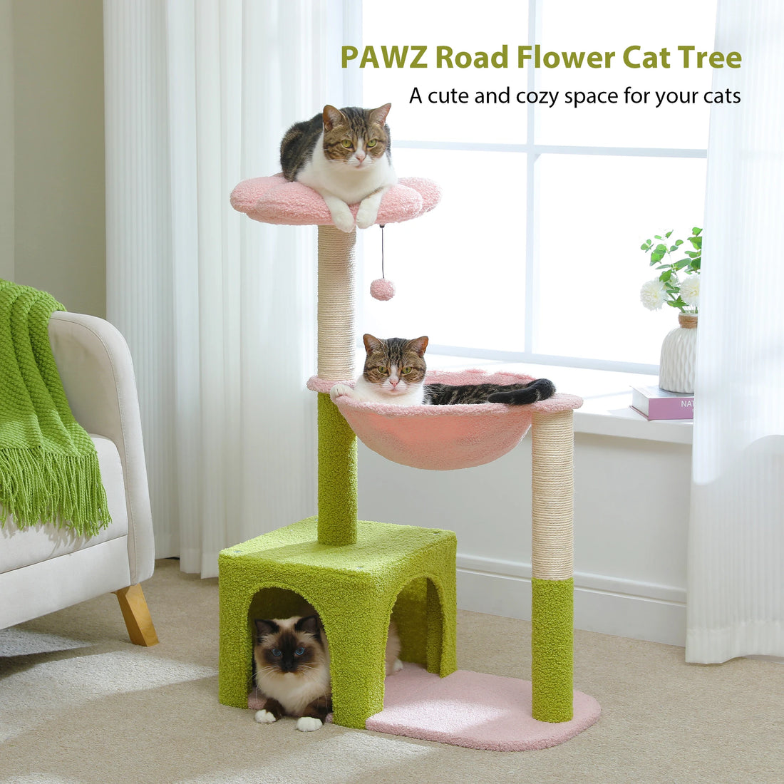 Arbre à chat fleur en coloris rose et vert avec trois chats, poteaux en sisal et pompon, placé devant une fenêtre