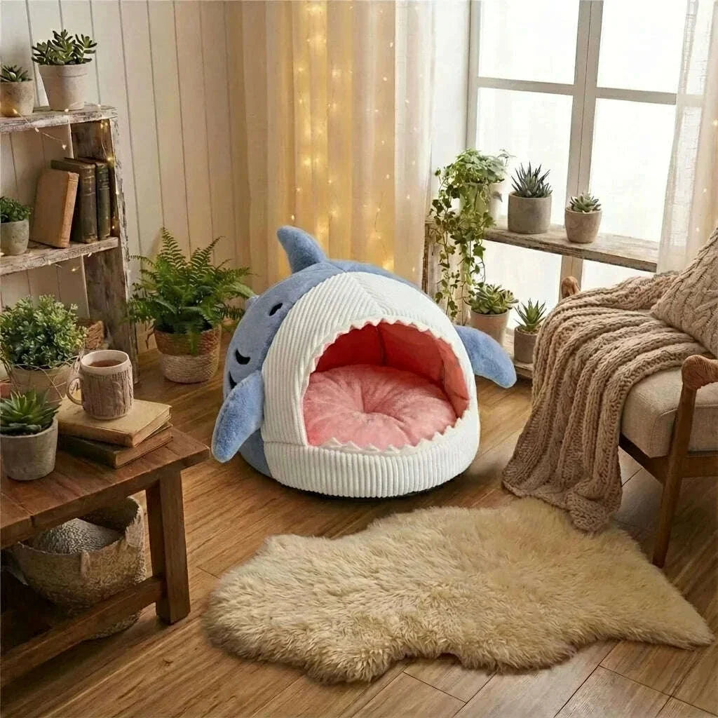 Abri douillet requin bleu et blanc posé sur un parquet, coussin rose rond visible, près d'un tapis en peau