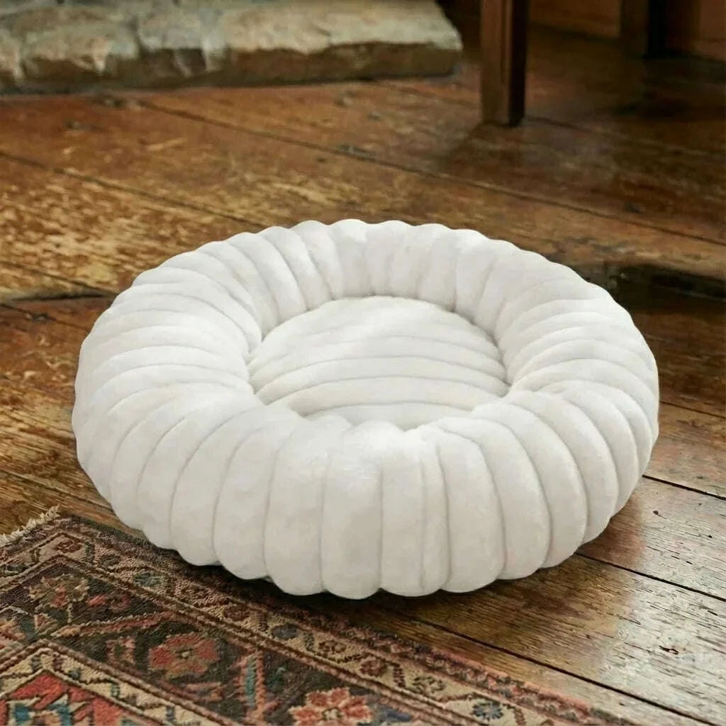 Corbeille ronde blanche pour chat aux boudins moelleux, posée sur un parquet ancien et un tapis
