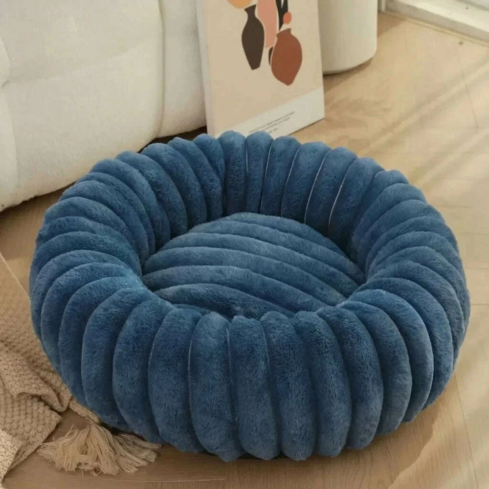 Corbeille ronde bleue en fausse fourrure à larges côtes, posée sur un parquet clair près d'un canapé blanc