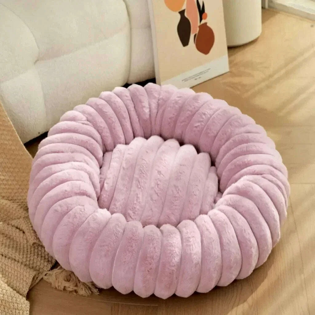 Couchage rond rose clair pour chat, bourrelet en peluche à gros bourrelets, au sol près d'un canapé blanc
