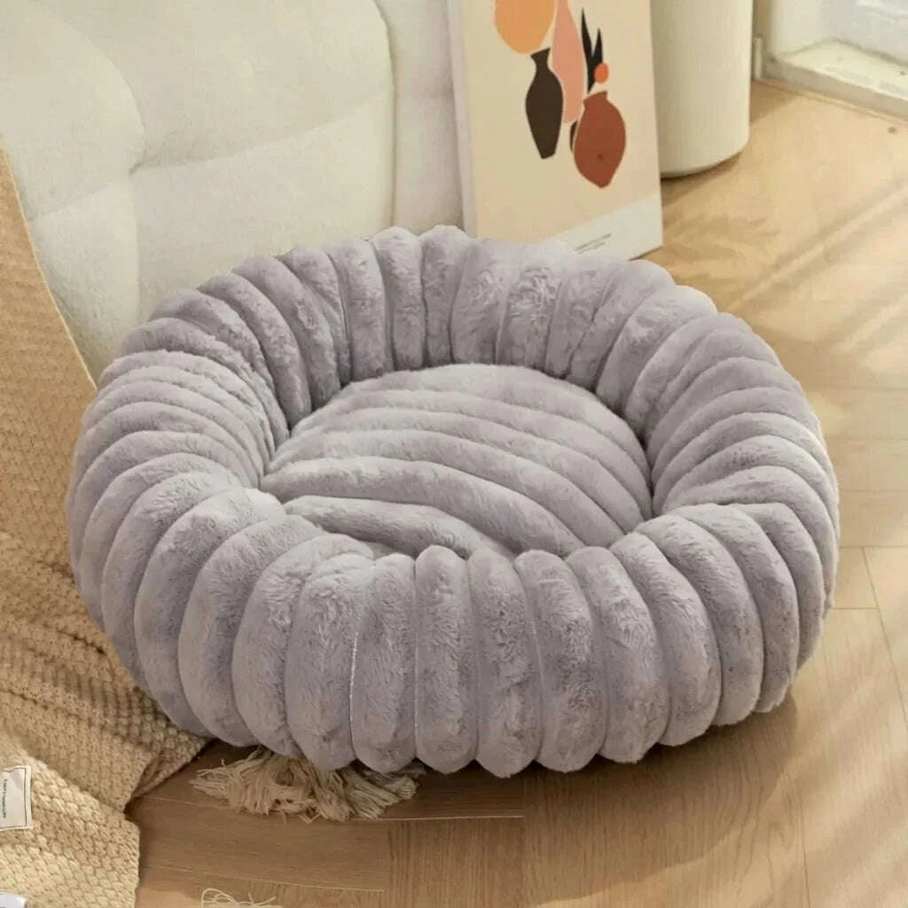 Détail du fond matelassé et du bord épais d'un lit rond gris pour chat, près d'un canapé et d'un plaid