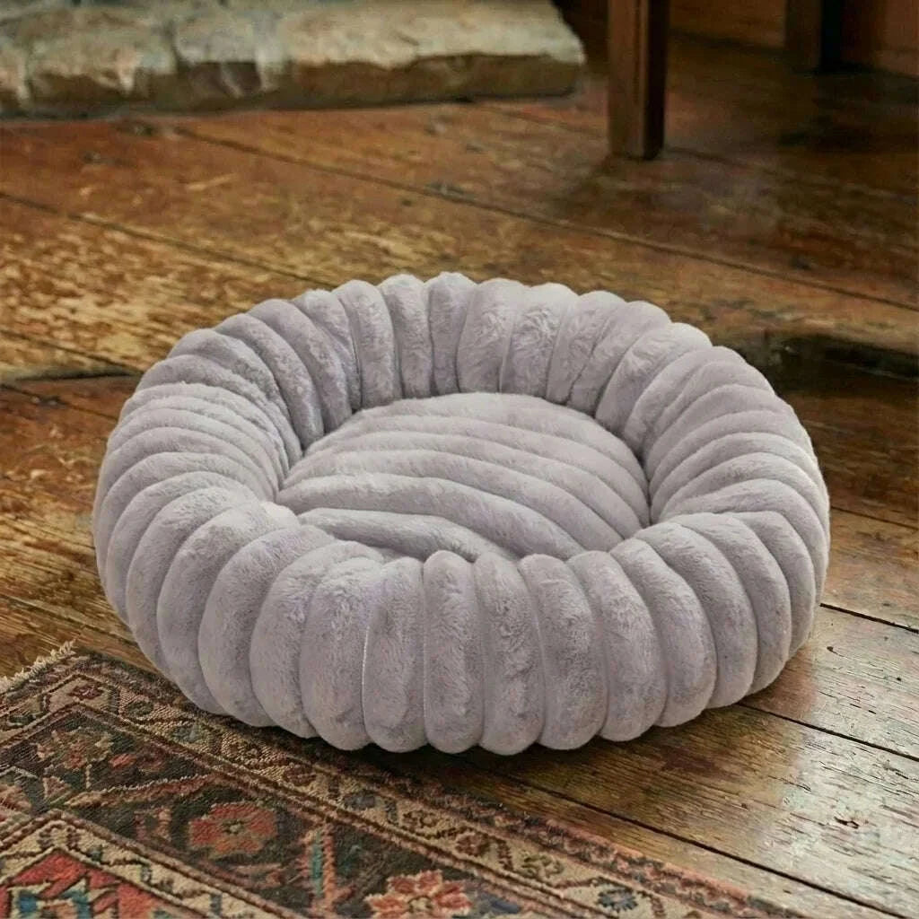 Couchage rond gris en fausse fourrure vide, posé sur un parquet ancien près d'un tapis à motifs