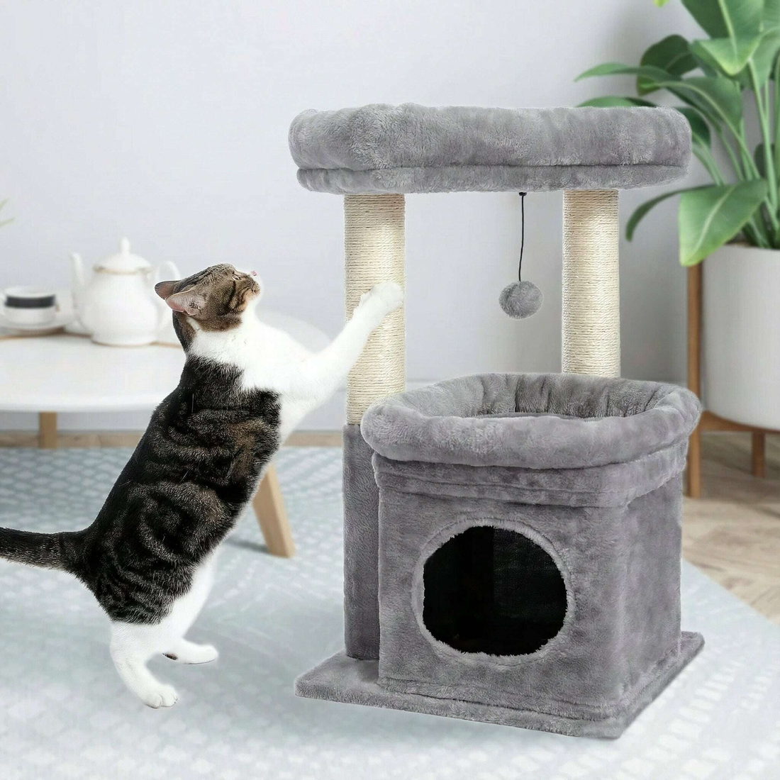Chat tigré et blanc dressé sur ses pattes arrière pour griffer le poteau en sisal d'un arbre à chat gris