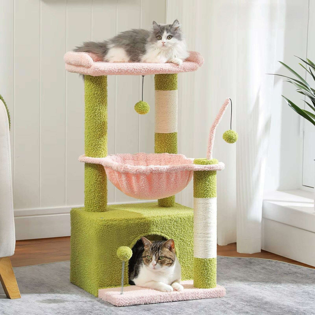 Griffoir sur pied vert et rose dans un salon, chat gris et blanc sur la plateforme, chat tigré dans la niche