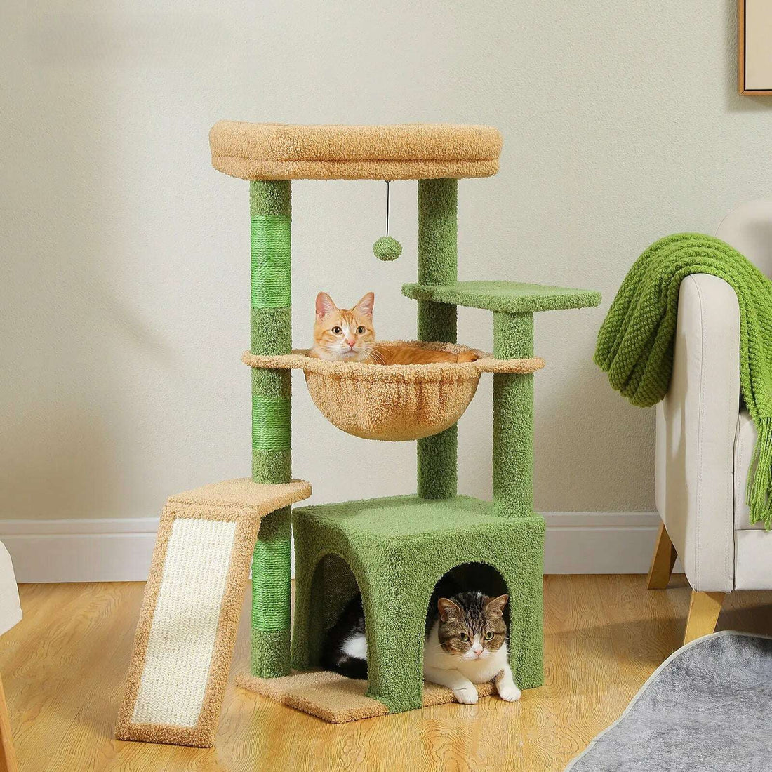 Chat roux dans le hamac d'un arbre à chat vert et sable, près d'un fauteuil crème et d'un plaid